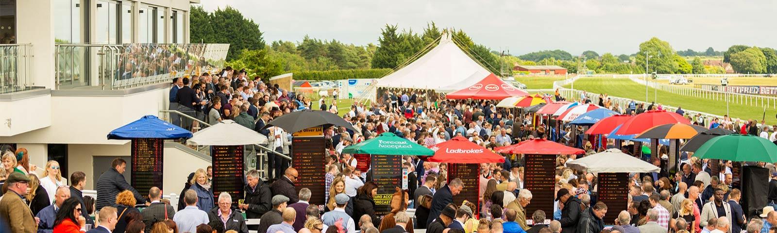 Crowds of racegoers gathered around bookmaker stands.
