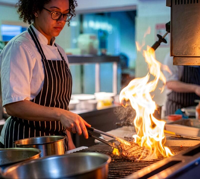 Chef cooking a steak on a grill.