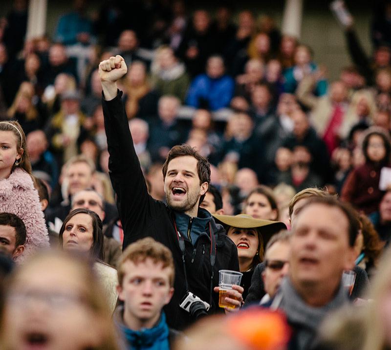 A man at the races cheering among the crowds.