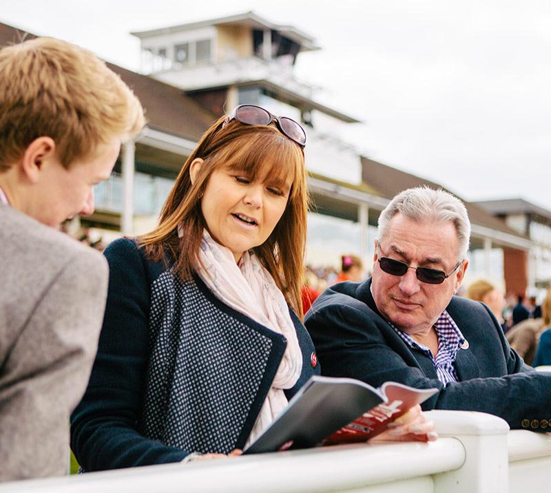 Three racegoers consulting over a racecard.