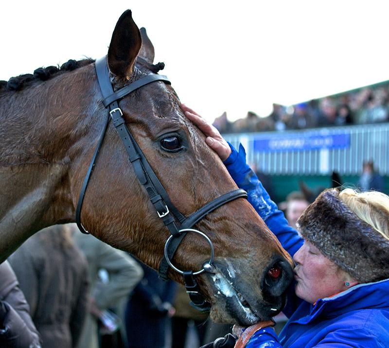 A lady kisses her horses nose.