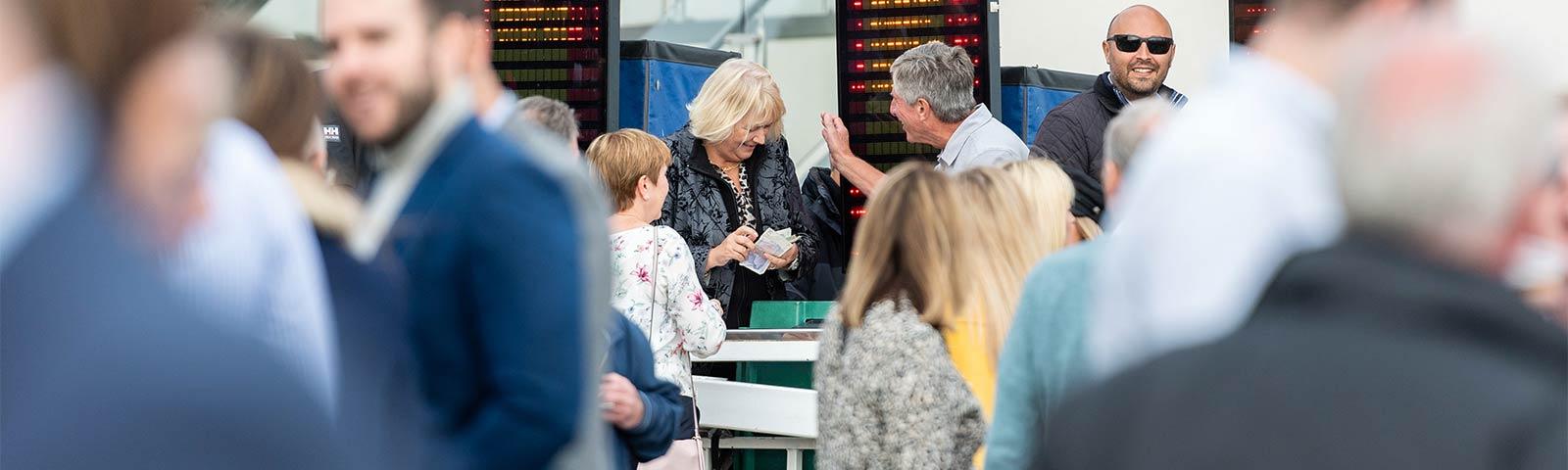 Crowds of people at the races, putting bets on the horses.